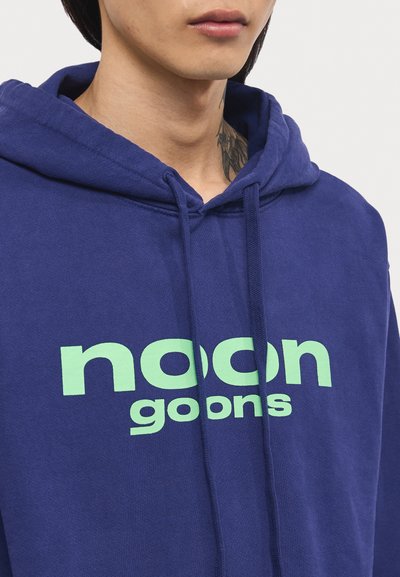 Navy Kapuzenpullover aus Baumwolle mit einem großen mintgrünen Grafikutext "noon goons" auf der Vorderseite. Mit einer Kordelzugkapuze und gerippten Bündchen.