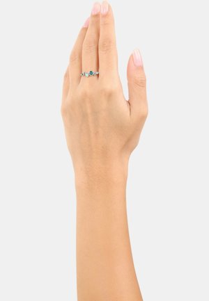 Anello d'argento con tre pietre di turchese, incastonato in una delicata fascia, indossato su una mano contro uno sfondo chiaro.