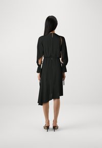 Crna haljina s dugim rukavima, suženim strukom, asimetričnom donjom ivicom i nabranim manžetama. Mekani materijal s glatkom teksturom i elegantnim padom.