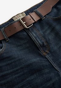 Ciemnoniebieskie dżinsy jeansowe mają gładką fakturę i pomarańczowe przeszycia, do których dołączony jest brązowy skórzany pasek ze srebrną klamrą.
