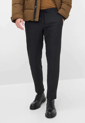 Schwarze tapered Hosen aus strukturiertem Stoff, mit einem Kordelzugbund und seitlichen Taschen, kombiniert mit schwarzen Schnürstiefeln.
