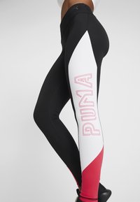 Legginsy w kolorystycznym bloku z czarnymi, białymi i czerwonymi panelami. Duże różowe logo "PUMA" na białej części. Gładki, elastyczny materiał.