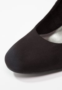 Chaussure plate noire pour femme à bout rond avec dessus en tissu lisse et petit talon sur fond blanc.