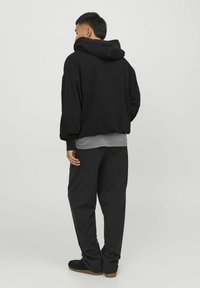 Sort oversized hættejakke med en stor hætte, parret med grå lag og sorte, løstsiddende bukser. Glat stof, minimalistisk design og afslappet stil.