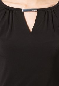 Top nero con maniche corte, caratterizzato da un collo a V e dettagli arricciati. Un accento in barra argentata sul colletto aggiunge un tocco elegante.