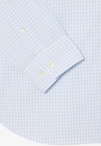 Manche de chemise à carreaux vichy bleu clair et blanc avec deux boutons transparents sur le poignet, posée à plat sur un tissu assorti en arrière-plan.