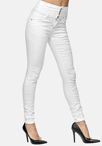 Jeans blancos de cintura alta con un acabado liso y texturizado, diseño de cinco bolsillos y cierre de tres botones, combinados con tacones altos negros.