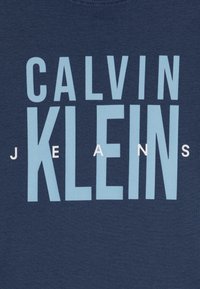 Camiseta azul marino con el texto en un vibrante azul claro "CALVIN KLEIN" y la palabra "JEANS" en blanco, sobre una suave tela de algodón.