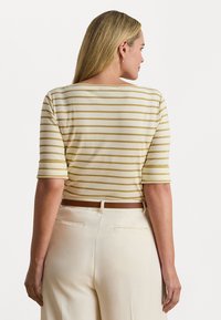 Prúžkovaný crop top v krémovej a jemne žltej farbe s krátkymi rukávmi. Má široký výstrih a je kombinovaný s vysokými krémovými nohavicami.