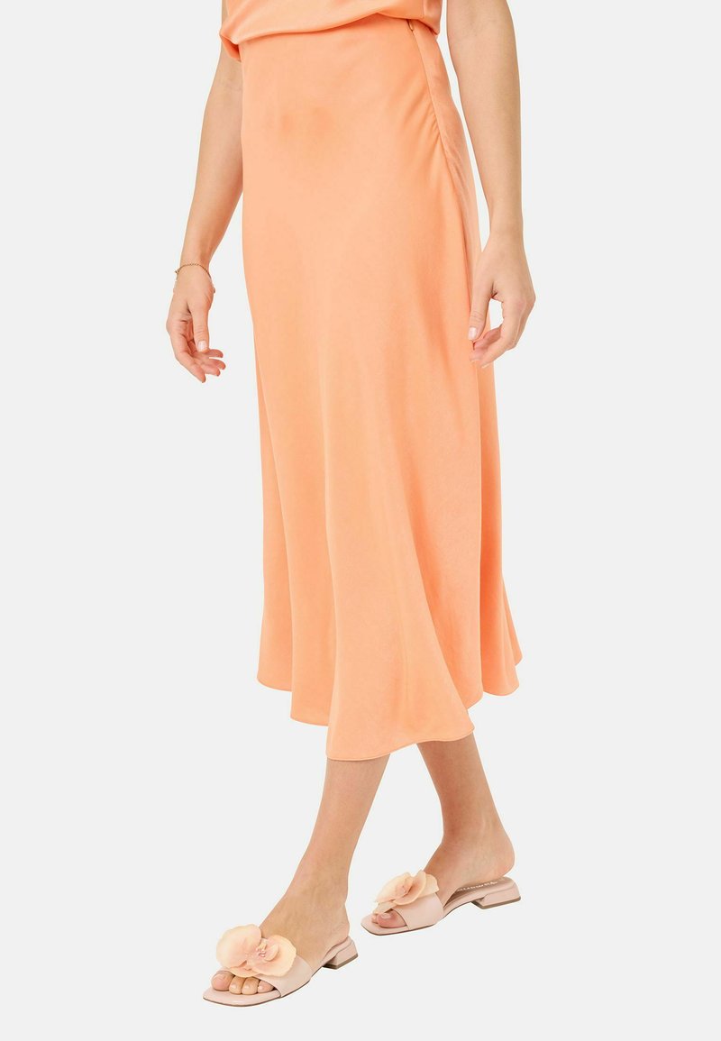Robe midi fluide de couleur pêche avec des fronces latérales, associée à des sandales à glisser rose clair avec des accents floraux et un talon plat.