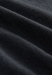 Textured dark fabric, primarily black, showing fine knit lines and subtle depth from folded layers, with a soft, smooth appearance.