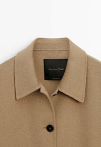 Beige wool coat with a structured collar, single black button closure, and tag displaying "Massimo Dutti." Soft texture and tailored design.