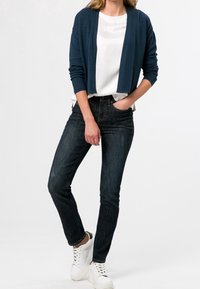 Navy knit cardigan over a white top, paired with dark blue skinny jeans and white sneakers. The outfit features a relaxed fit and simple design.