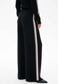Szerokie czarne spodnie z miękkiego materiału, z kontrastującym jasnobeżowym paskiem po boku i elastycznym pasem dla wygody.