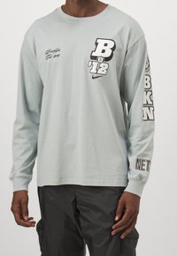 Langarm-T-Shirt in Hellblau aus Baumwolle, mit auffälligen schwarzen Grafiken, darunter "B" und "Brooklyn", in lockerer Passform.