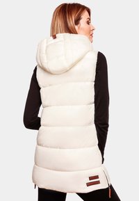 Gilet rembourré en crème clair avec une capuche amovible, présentant une texture matelassée et des poches zippées. Agrémenté d'étiquettes marron au bas.