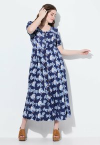 Námořnické květinové šaty s krátkými rukávy, kulatým výstřihem a knoflíky. Hladká látka má modro-bílé květinové vzory; v kombinaci s hnědými platformovými sandály.