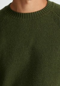 Pull en maille vert olive avec un col rond côtelé, présentant une texture douce et une coupe ajustée.