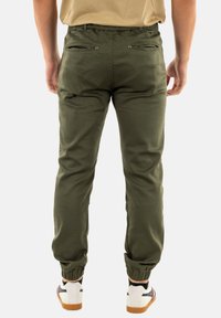 Pantalones jogger verde oliva con un corte ajustado, puños elásticos y dos bolsillos traseros con cremallera, hechos de una tela suave.