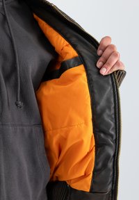Čierna kožená bunda s oranžovou prešívanou podšívkou. Obsahuje zips a rebrované detaily. Hladký povrch s precíznym prešitím.