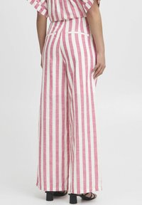 Wide-leg trousers in lightweight fabric, featuring vertical pink and white stripes, with back pockets and a high waist. Black heeled sandals visible.