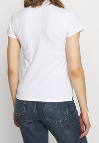 Weißes Baumwoll-T-Shirt mit kurzen Ärmeln und Rundhalsausschnitt. Hat einen geraden Saum mit Seitenschlitzen und eine strukturierte Oberfläche des Stoffs.