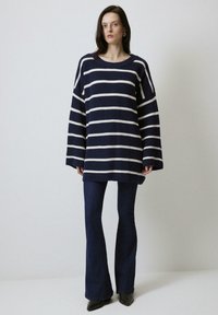 Pull en maille à rayures navy avec des manches larges, associé à un jean flare noir. Il arbore une coupe décontractée et un col rond.