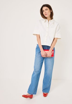 Witte T-shirt met korte mouwen en een kraag, voorzien van een voorzak, gecombineerd met lichtblauwe wijde jeans. Geaccentueerd met een rode clutch en schoenen.
