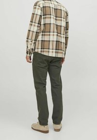 Camisa a cuadros marrón y crema combinada con pantalones verde oliva y zapatos beige, que muestra un corte relajado y un diseño de cuello estándar.