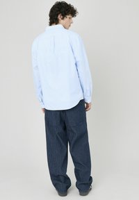 Chemise boutonnée à rayures bleu clair avec une coupe décontractée, associée à un pantalon large en bleu foncé présentant un motif texturé et deux poches arrière.