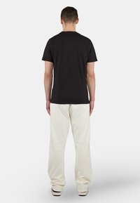 Camiseta de algodón negra combinada con pantalones de chándal blancos. La camiseta tiene un cuello redondo clásico y los pantalones de chándal presentan un ajuste suelto y relajado.