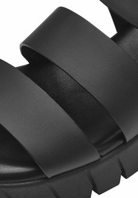 Black sandals with wide, smooth leather straps and a textured footbed, featuring a chunky rubber sole with deep grooves for traction.