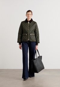 Gequiltede groene jas met een bruine kraag, ritssluiting en twee voorzakken. Gecombineerd met donkere jeans en een grote zwarte handtas.
