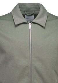 Hellgrüne Jacke mit Reißverschluss vorne, strukturiertem Kragen und texturiertem Stoff. Verfügt über ein Logoetikett auf der Innenseite des Kragens zur Markenkennzeichnung.