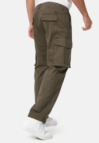 Olive green cargo pants feature multiple pockets, tapered legs, and are made from a durable cotton blend. Worn with white sneakers.