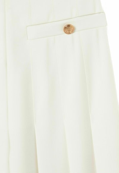 Pantalones blancos con pliegues que presentan un botón dorado en la cinturilla, con una textura suave y un diseño ajustado.