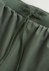 Badeshorts med elastisk talje i mørkegrøn stof med snøre. Glat tekstur, enkelt design, forstærket syning ved toppen.