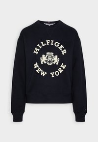 Svart sweatshirt med rundad hals, långa ärmar och ribbade muddar. Har en krämfärgad "HILFIGER NEW YORK"-logotyp och skölddesign.