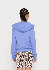 Ljusblå kort hoodie med stor huva, ribbade muddar och en avslappnad passform, kombinerad med cykelshorts i leopardmönster.