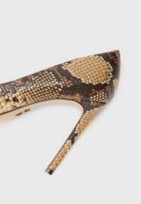 Cipele na visokom potpetici s oštrim vrhom, s uzorkom smeđe i bež zmijske kože i elegantnom crnom stiletto potpeticom.
