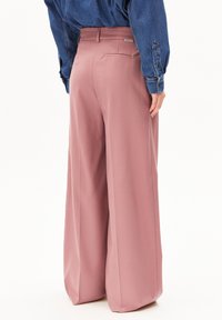 Brede pijpen broek van zacht roze stof, met een tailleband, zijzakken en een gladde textuur. Een spijkerhemd wordt gedragen voor contrast.