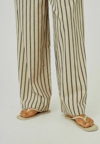 Beige striped wide-leg pants with black vertical lines, textured fabric, paired with simple beige flip-flops and exposed toes.