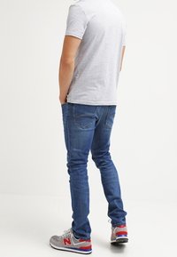 Blå denimjeans med smal passform, med bakfickor och en subtil blekning. Matchas med grå och röda sneakers och en grå t-shirt.
