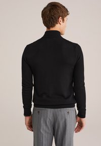 Schwarzer Strickpullover mit Polo-Kragen, mit tailliertem Schnitt und gerippten Bündchen. Getragen mit grauen gestreiften Hosen, Rückansicht.
