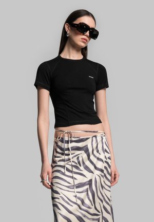 Schwarzes Kurzarm-Crop-Top mit körpernahem Schnitt und feiner Naht, kombiniert mit einem cremefarbenen Rock mit grauem Zebramuster und Bindegürtel.
