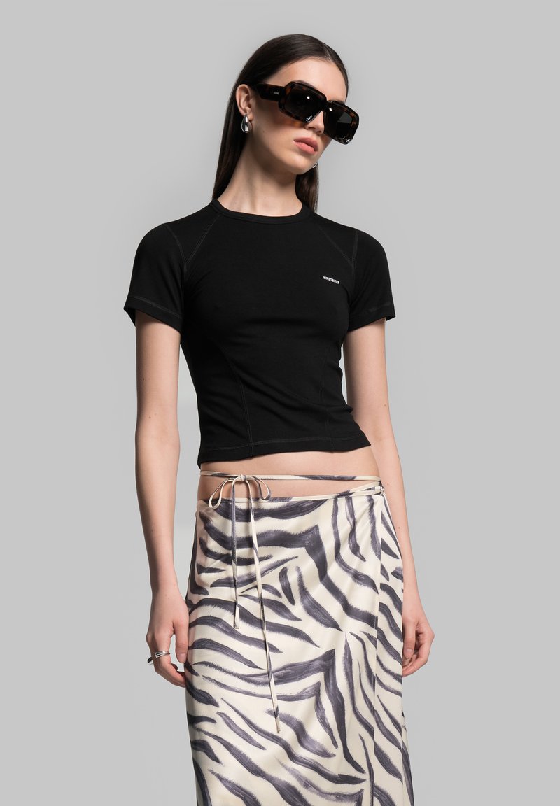 Black short-sleeve crop top with fitted design and light stitching, paired with a cream skirt featuring a grey zebra stripe pattern and tie waist.
