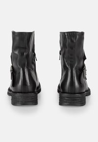 Botas de tobillo de cuero negro con un acabado liso, tacón robusto apilado, cremalleras laterales y acentos ajustables con hebillas para un detalle adicional.
