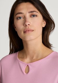 Roze top met korte mouwen en een ronde halslijn, voorzien van een keyhole-detail, een gladde textuur en minimale stiksels. Eenvoudig en strak ontwerp.