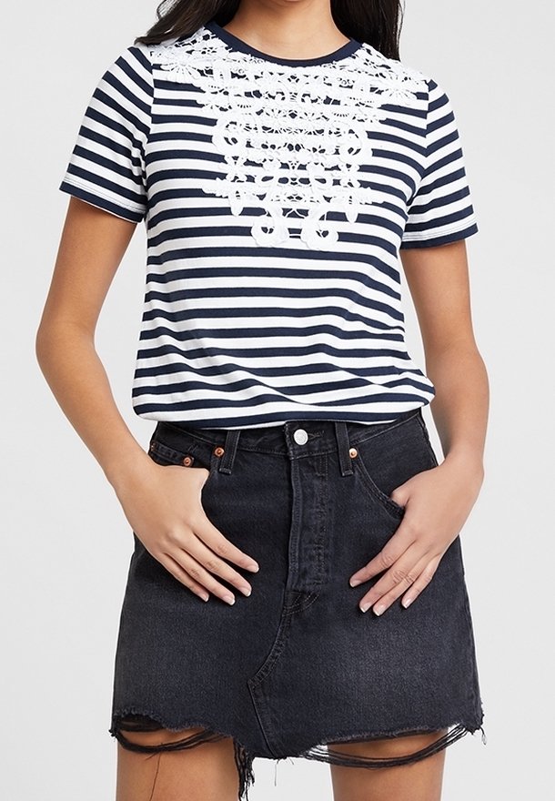 Laivastonsininen ja valkoinen raidallinen T-paita, jossa on pitsiyksityiskohtia kaula-aukossa, yhdistetty korkeavyötäröiseen mustaan farkkuhameeseen, jossa on revitty helma.