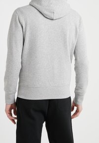 Sudadera gris hecha de material suave con un ajuste relajado, con capucha ajustable y puños y dobladillo acanalados, combinada con pantalones negros.
